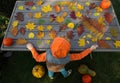 unrecognizable hooded boy playing with many beautiful bright colorful autumn leaves laid out on the table