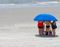 Unrecognizable ladies crowed under a beach umbrella trying to get out of the hot summer sun on a South Carolina beach.