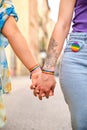 Unrecognizable lesbian couple holding hands with LGBTQ flag bracelets and pin. Royalty Free Stock Photo