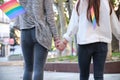 Unrecognizable lesbian couple holding hands wearing LGBT bracelets and with LGBT flags in their pockets.