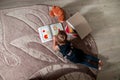 Unrecognizable little girl in a dark blue dress reading book lying on the floor near teddy bear. Child reads story for toy. Top v Royalty Free Stock Photo