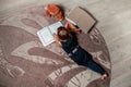 Unrecognizable little girl in a dark blue dress reading book lying on the floor near teddy bear. Child reads story for toy. Top v Royalty Free Stock Photo