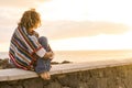 Unrecognizable lonely woman sit down on a wall looking and enjoying the sunset on the sea - coloured trendy mexican poncho style Royalty Free Stock Photo