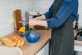 Unrecognizable man breaking egg with knife into blue plastic bowl near steel colander. Cooking. Royalty Free Stock Photo