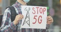 Unrecognizable man in face mask holding Stop 5G banner outdoors. Male Caucasian demonstrator protesting against harmful