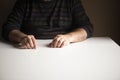 Unrecognizable man in a familiar position sitting at a white empty table, focus on his hands