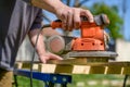 Unrecognizable man in the garden sanding wooden planks. DIY home improvement, restoration, carpentry concept. Royalty Free Stock Photo