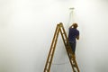 Unrecognizable man on ladder back view paints white wal