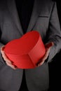 Unrecognizable man in suit holds out heart shaped gift red box  congratulatory concept  black background Royalty Free Stock Photo