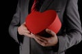 Unrecognizable man in suit holds out heart shaped gift red box  congratulatory concept  black background Royalty Free Stock Photo