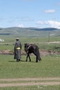 Unrecognizable man with traditional mongolian clothes walking next to his horse Royalty Free Stock Photo
