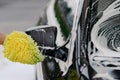 Unrecognizable man washes black car with cloth or rag mitten, uses special detergent. Cleaning dirty automobile. Carwash business