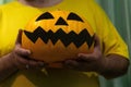 An unrecognizable man in a yellow t-shirt holds an orange Jack pumpkin with a gruesome painted face for Halloween. Angry smiling p Royalty Free Stock Photo