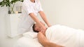 Unrecognizable masseuse giving shoulder massage to elderly man relaxing on massage table in luxury white spa beauty clinic. Royalty Free Stock Photo