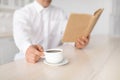 Unrecognizable mature man drinking coffee and reading book, enjoying peaceful morning at home, selective focus, crop Royalty Free Stock Photo