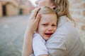 Unrecognizable mother consling her little daughter crying, holding her in arms in street in summer. Royalty Free Stock Photo