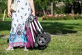 Unrecognizable mother holding folded baby pushchair, standing on green grass in meadow in summer park, copyspace