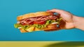 Unrecognizable person holding delicious sandwich with ham, tomatoes, cucumber and cheese slices and fresh lettuce on blue Royalty Free Stock Photo