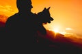 Unrecognizable person holding a dog. Silhouette against sundown