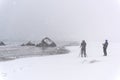 Person photographing a rock on the beach during a windy snowstorm