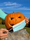 Unrecognizable person puts a covid medical face mask on carved Halloween pumpkin Royalty Free Stock Photo