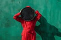 Unrecognizable person in red outfit hiding face behind big round clock with black dial. A human in red suit with big