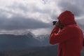 Unrecognizable photographer in a red coat taking a picture of a cloudy landscape