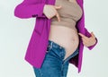 Unrecognizable pregnant woman in not buttoned denim pointing fingers at big belly, problems during pregnancy