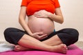 Unrecognizable pregnant woman training yoga in lotus pose, caressing her belly Royalty Free Stock Photo