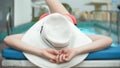 An unrecognizable slim busty woman in a big white hat and a pink bikini is lying on a chaise lounge near the pool. her Royalty Free Stock Photo