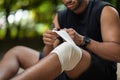 Unrecognizable sportsman sitting on the ground, wrapping injured knee