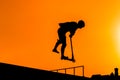 Teenager silhouette showing high jump tricks on scooter against orange sky Royalty Free Stock Photo