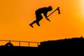 Teenager silhouette showing high jump tricks on scooter against orange sky Royalty Free Stock Photo