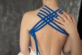 Unrecognizable therapist doctor massaging applying blue kinesio tapes with hand on bare back spine of woman patient.