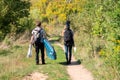 Unrecognizable travelers with backpack, guitar and sup board going through green countryside road