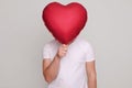 Unrecognizable unknown man holding red helium balloon in heart shape in front of his face guy wearing white casual T-shirt Royalty Free Stock Photo