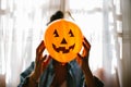 Unrecognizable Witch holding a pumpkin balloon with her hand and covering her face. Young woman celebrating halloween. Helium