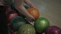 Woman approaches rollout system in bowling alley and takes orange ball.