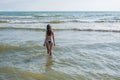 Unrecognizable woman with long hair in blue bikini walking down the water on the seaside. Back view.