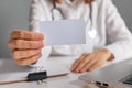 Unrecognizable woman doctor holding empty business or visit card offering her medical services doctor wearing white lab coat and Royalty Free Stock Photo