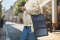 Unrecognizable woman with flexible solar battery holding smartphone in background of a city.