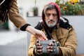 Unrecognizable woman giving money to homeless beggar man sitting in city.