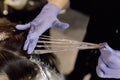 Unrecognizable woman hairdresser colorist hold strand of long hair, distributing hair dye with fingers in blue gloves.