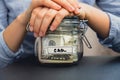 Unrecognizable woman holding Saving Money In Glass Jar filled with Dollars banknotes. CAR transcription in front of jar