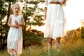 Unrecognizable woman, mother in hat and little blonde daughter in light white dresses walking together in natural forest