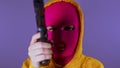 Unrecognizable woman in pink balaclava with gun on purple background. Dangerous female in mask takes aim at camera