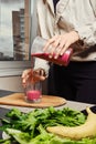 Unrecognizable woman pouring banana and black currant smoothie in glass