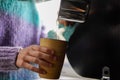 unrecognizable woman pouring boiling water from a pot into a bamboo cup at a campsite in winter