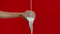 Unrecognizable woman pouring milk into glass in studio on red background.