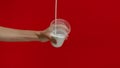 Unrecognizable woman pouring milk into glass in studio on red background.